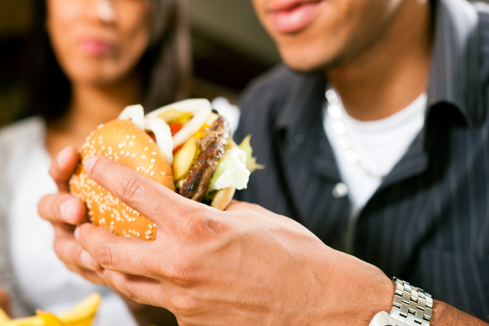 Man in a fast food restaurant eating a hamburger with his girlfriend