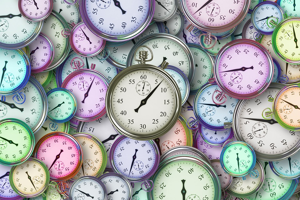 Multiple clocks of various colors and sizes laying on a flat surface